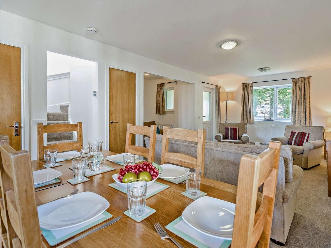 A dining area with wooden chairs, a table set for four, and a bowl of fruit.