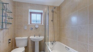 A bathroom with a toilet, sink, and bathtub, tiled in beige, with a window above the sink. - 2 Bed in Bideford (oc-85890) (Westward Ho!)
