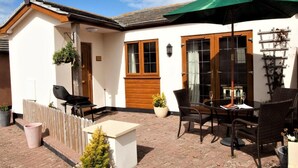 A patio with a table and chairs, a green umbrella, and potted plants. - 2 Bed in Bideford (oc-85890) (Westward Ho!)