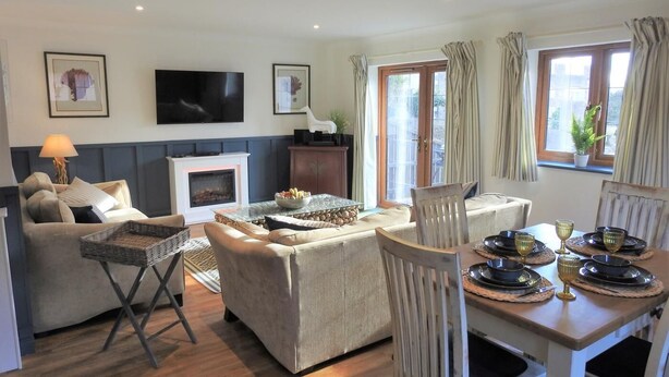 A living room with a fireplace, sofa, dining table, and TV. - 2 Bed in Bideford (oc-85890) (Westward Ho!)