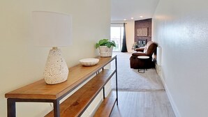 Un interior modern amb una banca de fusta, una làmpada blanca i una planta en test.