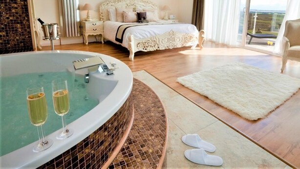 Une chambre avec un grand lit, une baignoire et des coupes à champagne, ainsi qu’un balcon avec vue.