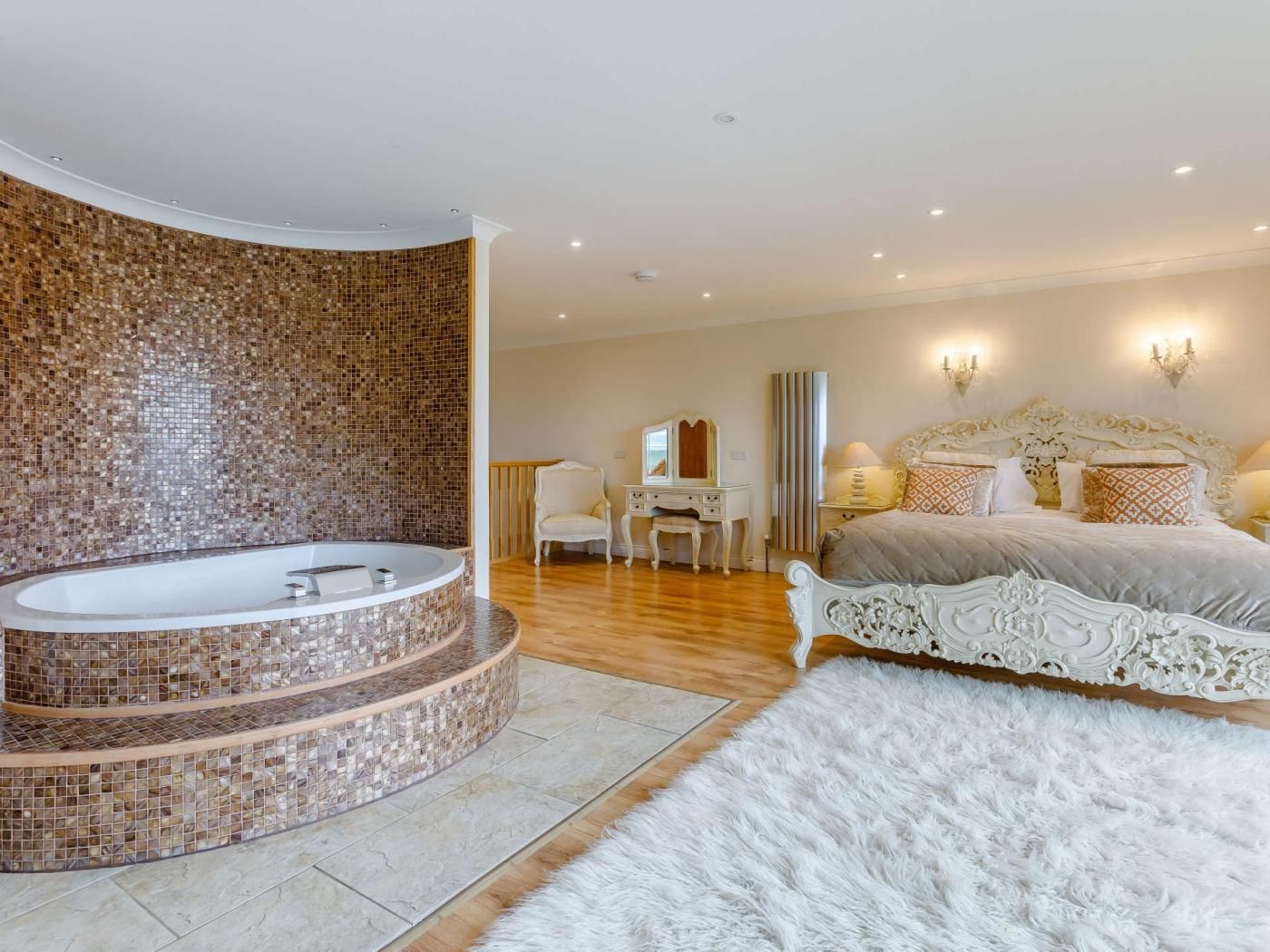 Een slaapkamer met een rond jakuzi, een groot bed, een kaptafel met spiegel en een bureau.