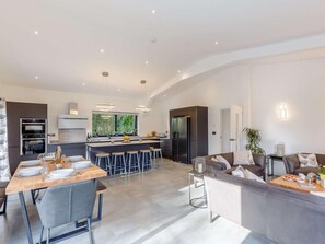 Een moderne keuken met een centraal kookeiland, barkrukken en een eethoek met een tafel voor vier personen.