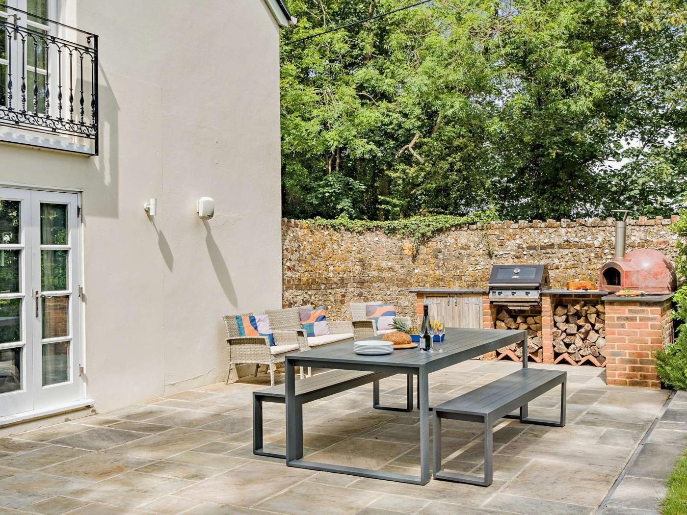 En udendørs terrasse med et bord, bænke, grill og pizzaovn.