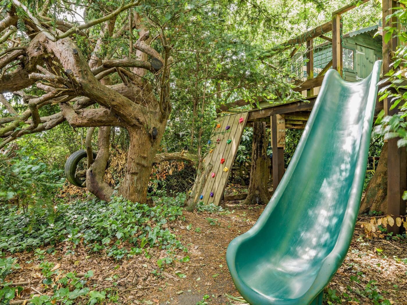 Un parque infantil con tobogán, pared de escalada y un árbol.