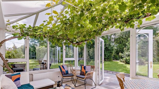Ein Wintergarten mit Korbmöbeln, einem Esstisch und Blick auf einen Garten.