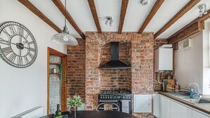 Eine Küche mit Backsteinwand, Holzbalken, einer Uhr und einem Esstisch mit Brot.