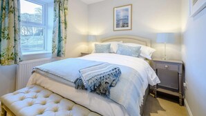Ein Schlafzimmer mit einem Bett, Nachttischlampen, einem gerahmten Bild an der Wand und einem Fenster mit Vorhängen.