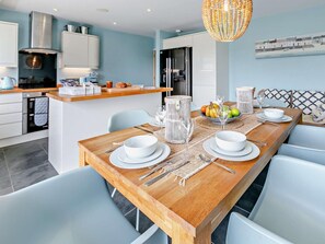 A modern kitchen with white cabinets, a wooden island, and a dining area with a long table set for four. - 3 Bed in Braunton (oc-86078) (Croyde)