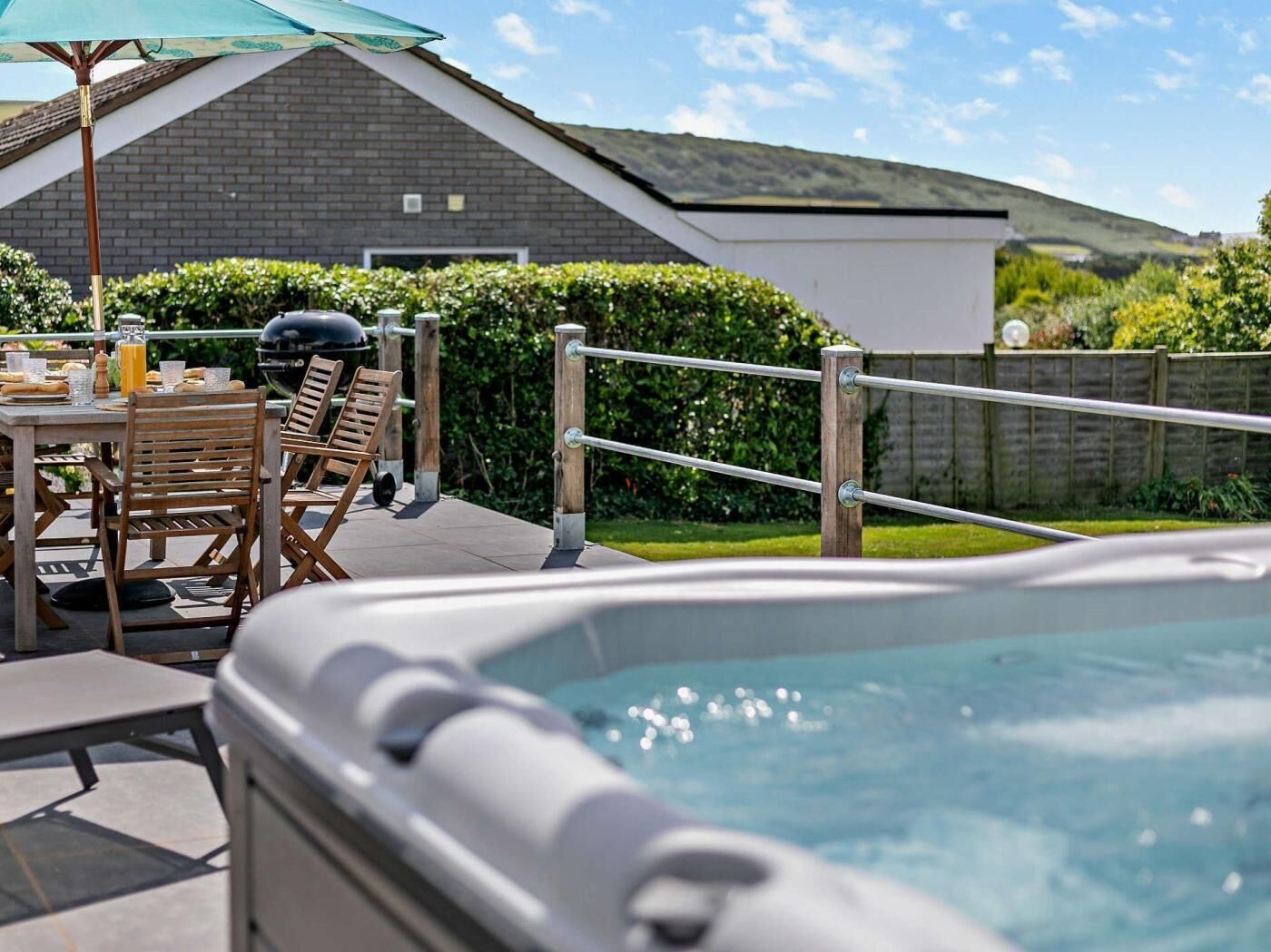 Un bain à remous avec une terrasse en bois, une table avec des chaises et un barbecue.