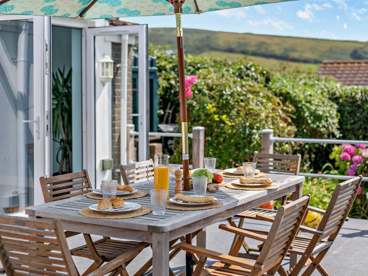 An outdoor dining area with a table set for two, surrounded by wooden chairs.