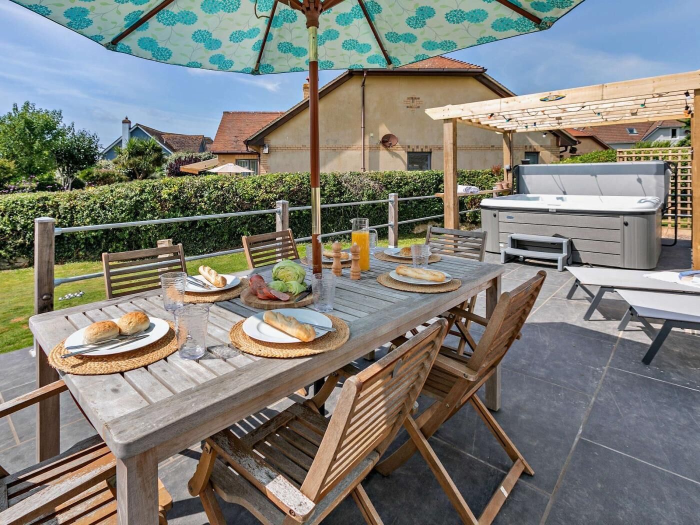 Un área de comedor al aire libre con una mesa de madera, sillas y un paraguas grande.