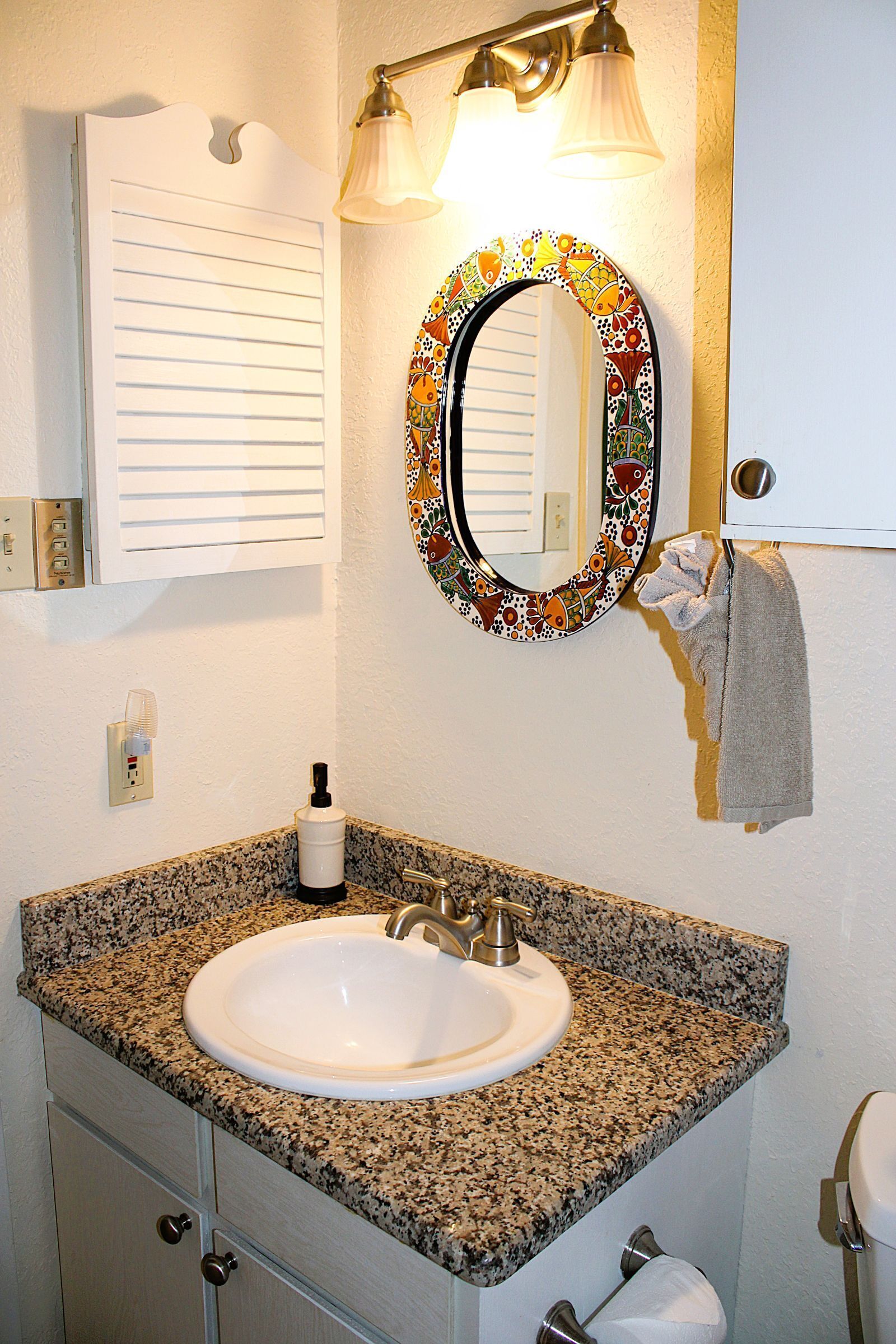 A bathroom with a granite countertop sink, a mirror with a decorative frame, and a towel hanging on the wall.