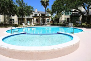 A swimming pool with two separate sections, surrounded by a fence, with lounge chairs and a covered seating area in the background. - Rockport Racquet and Yacht Club - 68 (Rockport)