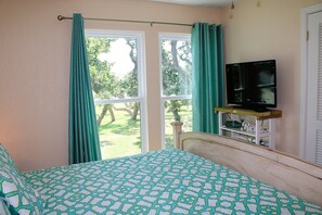 A bedroom with a bed, a television on a wooden stand, and a window with curtains. - Rockport Racquet and Yacht Club - 68 (Rockport)