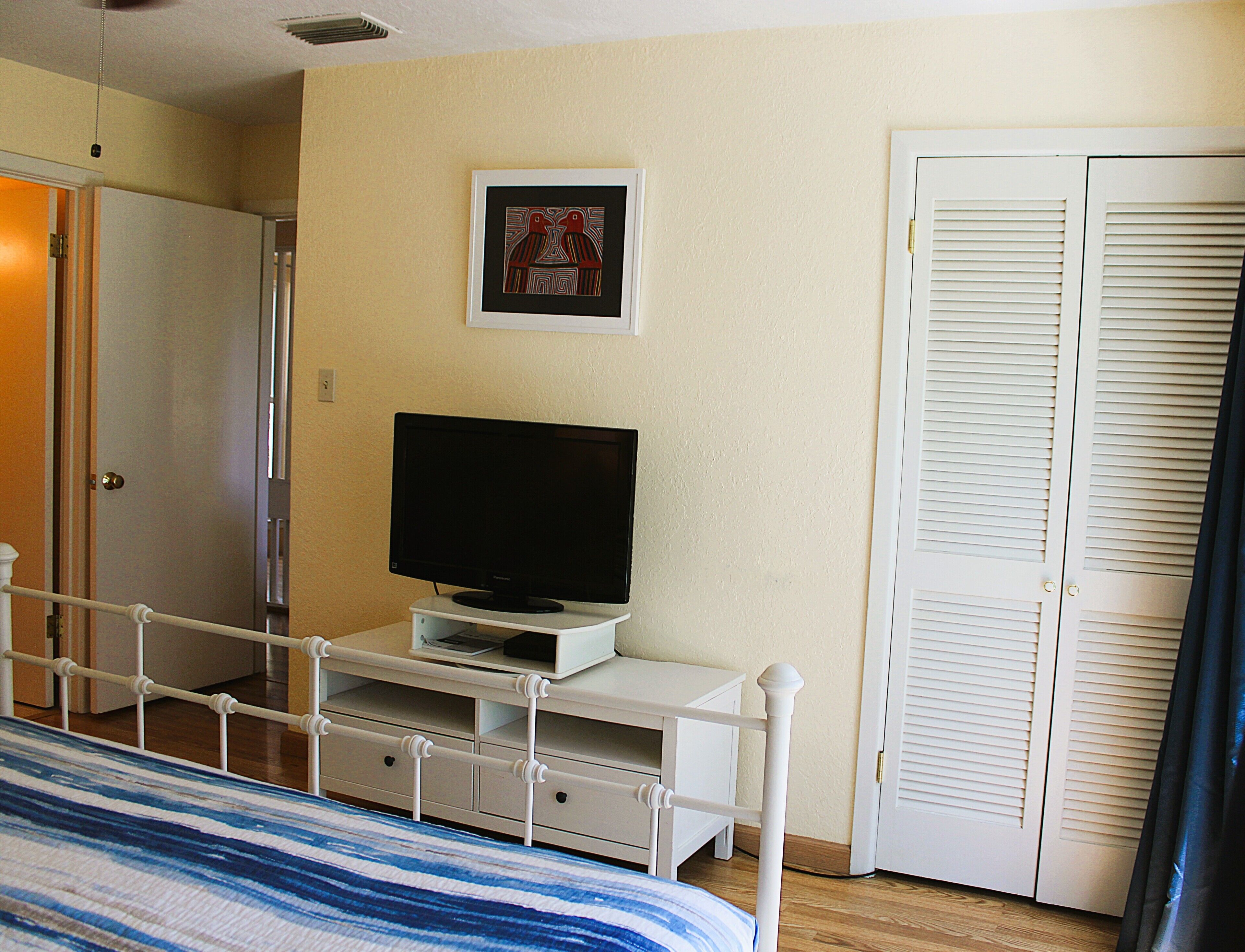 A room with a bed, a television on a stand, a door, and a framed picture on the wall.