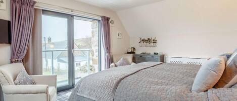 Une chambre avec un grand lit, une chaise, une commode et une vue par la fenêtre.