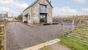 A stone building with a modern glass entrance, a gravel driveway, and a wooden fence.