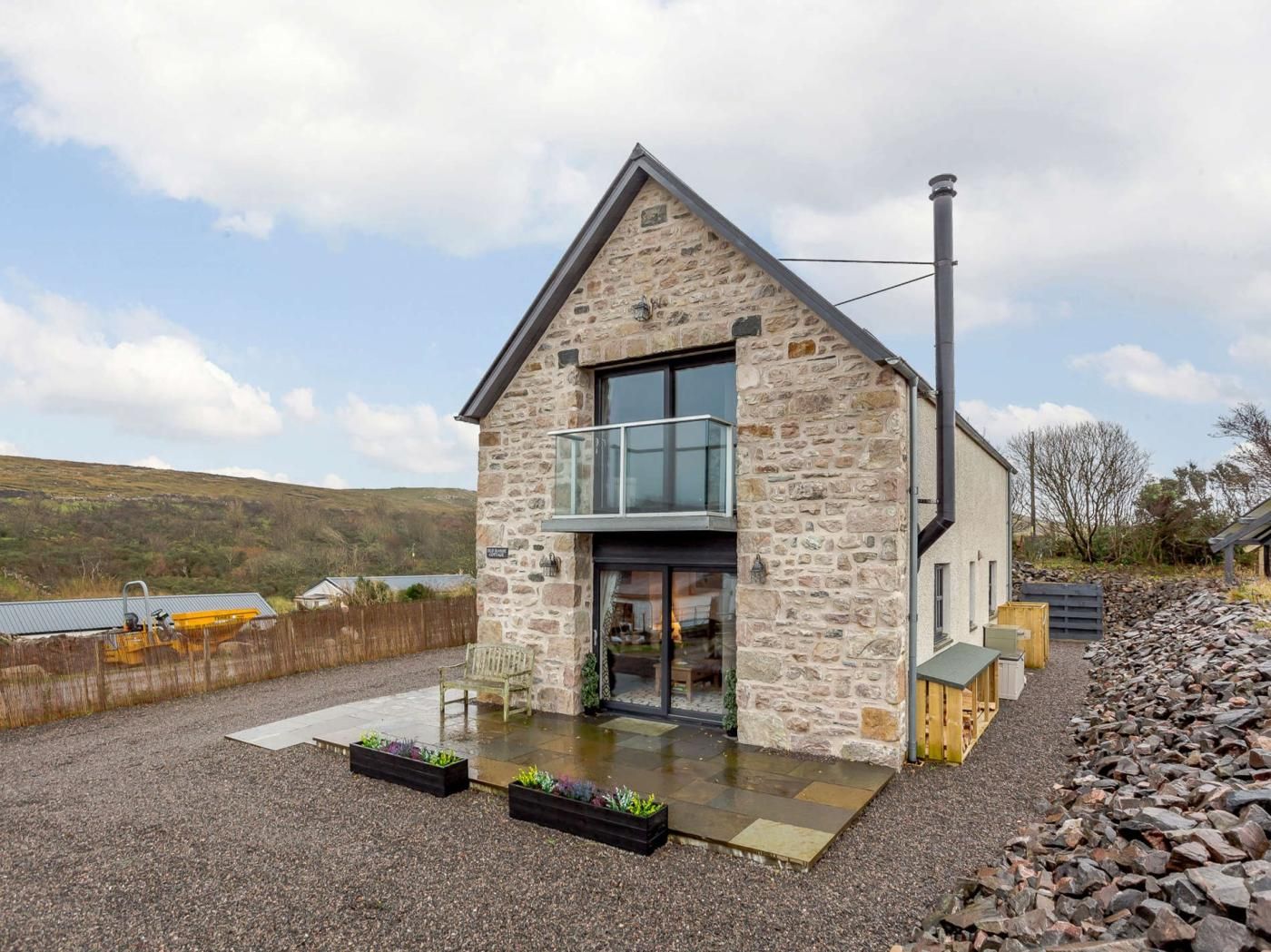 A stone house with a balcony, a large window, and a gravel driveway.