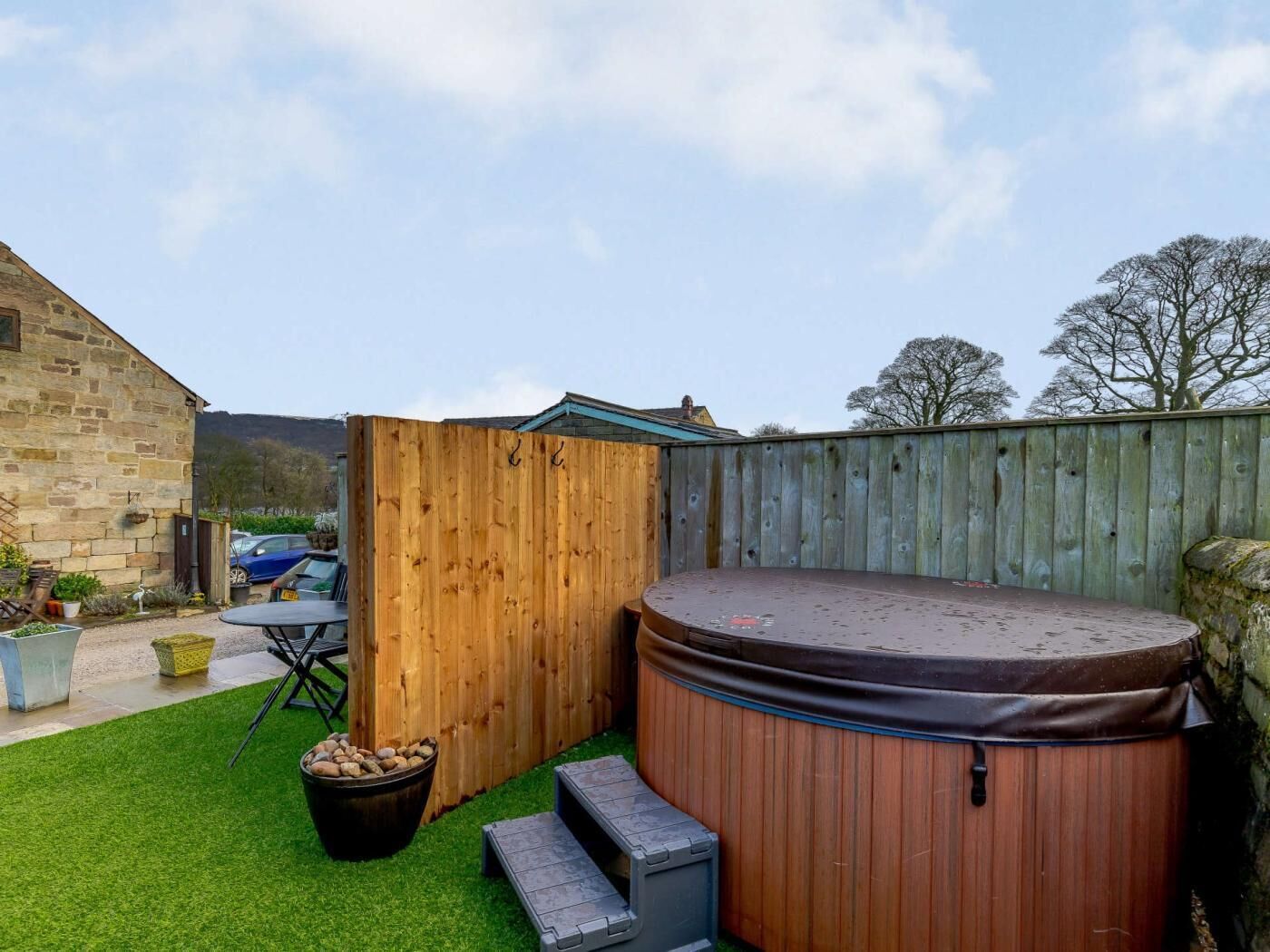 A backyard with a hot tub, a wooden fence, a stone wall, and a stone building.