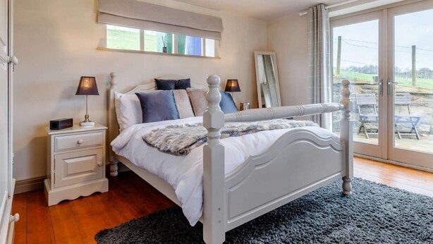Une chambre à coucher avec un lit, des tables de chevet, un miroir et une vue sur l’extérieur par une grande fenêtre.