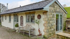Un bâtiment en pierre avec un toit en pente, un banc et un petit espace aménagé en jardin.