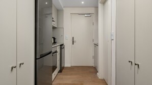 A narrow hallway with a kitchen area on one side, featuring cabinets, a refrigerator, and a microwave. - Bella at Dolce Vita | Stylish Sea Point Studio (Cape Town)