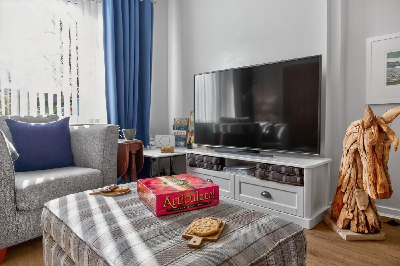 A living room with a sofa, a coffee table with a board game, a TV, and a wooden sculpture.