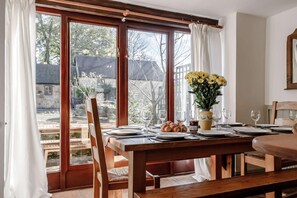 Ein Essbereich mit Tisch für vier Personen, einer Vase mit gelben Blumen und Blick durch große Fenster nach draußen.