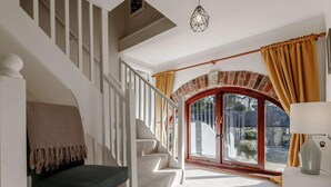 Una escala amb una cadira, una làmpada i una vista a través d'una porta de vidre amb cortines.