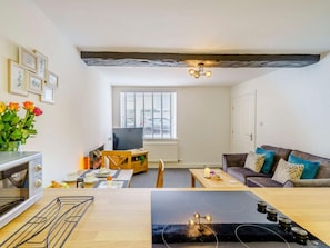 Ein modernes Wohnzimmer mit einem Flachbildfernseher, einem Holzesstisch und einer Couch mit Kissen.