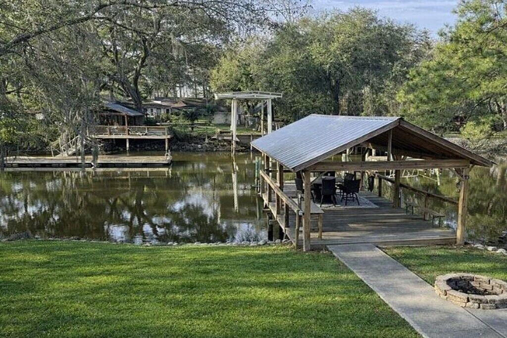 Un muelle de madera que se extiende sobre un lago tranquilo, un pabellón y un edificio pequeño con terraza.