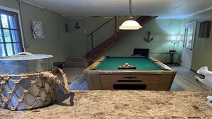 A pool table in a room with a staircase, a hanging light fixture, and a decorative anchor on the wall. - Wight Tide Landing (Midway)