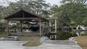A wooden pavilion with a roof, a dock extending into a body of water, and a stone fire pit. - Wight Tide Landing (Midway)