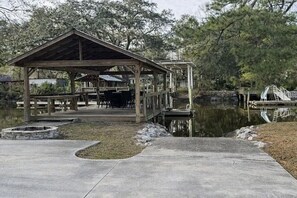 A wooden pavilion with a roof, a dock extending into a body of water, and a stone fire pit. - Wight Tide Landing (Midway)