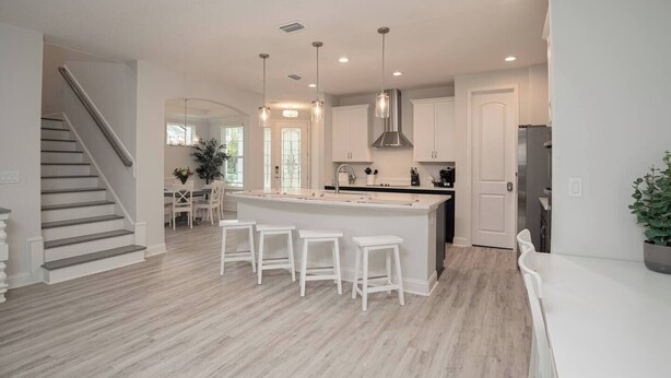 Una cocina moderna con una isla central, taburetes blancos y una escalera que lleva a otra habitación.