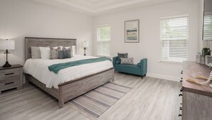 Un dormitorio con una cama de madera, mesitas de noche, un sofá y un ventanal con persianas.