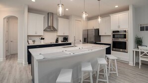 Una cocina moderna con armarios blancos, electrodomésticos de acero inoxidable y una isla central con taburetes de bar.