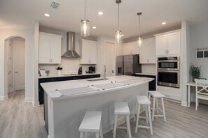 A modern kitchen with white cabinetry, stainless steel appliances, and a central island with bar stools. - Close to Vilano Beach - Private Hot Tub (St. Augustine)
