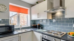 A modern kitchen with a dishwasher, microwave, stove, oven, and a window with an orange blind. - 1 Bed in Hornsea (oc-85722) (Hornsea)