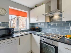Cocina moderna equipada con lavavajillas, microondas, estufa, horno y una ventana con persiana naranja.