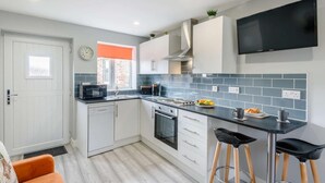 A modern kitchen with white cabinets, a black countertop, and a built-in oven. There are two bar stools and a clock on the wall. - 1 Bed in Hornsea (oc-85722) (Hornsea)