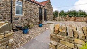 A stone building with a red-tiled roof, a window, and a door. There are two potted plants and a stone wall in the foreground. - 1 Bed in Hornsea (oc-85722) (Hornsea)