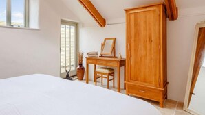 Quarto com claraboia, vigas de madeira no teto, cama, escrivaninha com cadeira e guarda-roupa.