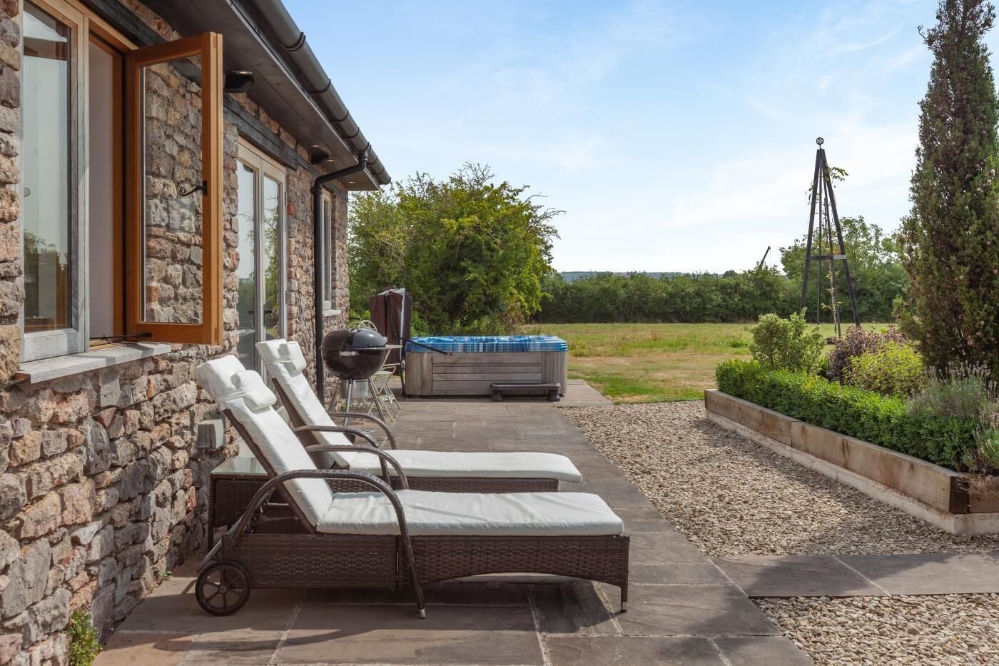 A stone building with a patio area featuring lounge chairs, a hot tub, and a grill.