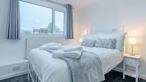 Une chambre à coucher avec un lit, une table de chevet, une fenêtre avec des rideaux et un radiateur.