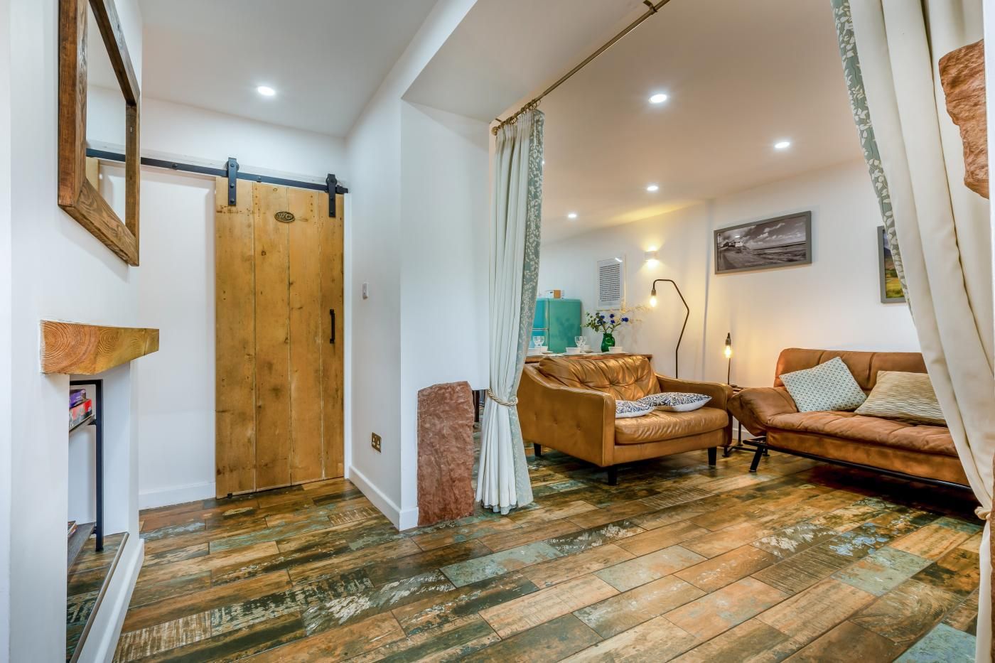 Un salon avec un canapé en cuir marron, une porte en bois et un tapis à motifs.