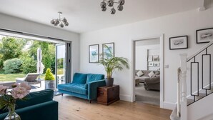 Uma sala de estar ampla, com sofá azul-turquesa, piso de madeira e uma janela grande.