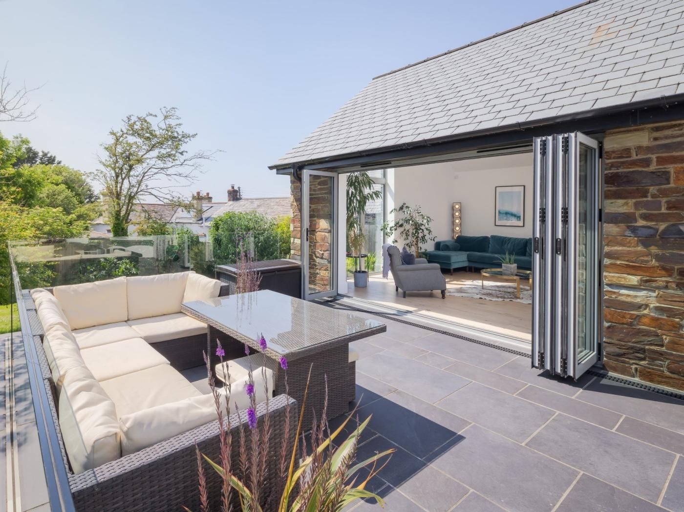A modern outdoor patio with a glass enclosure, a sofa, and a dining table.